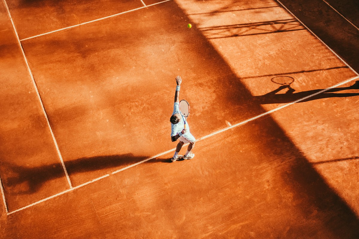 Tennisspelare i uppseende under en serve på grusbana