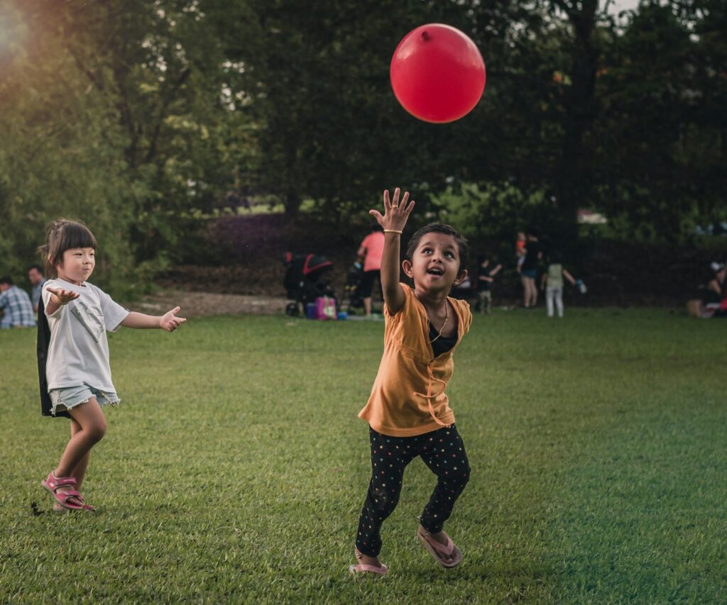 Barn leker med en röd ballong på en gräsmatta